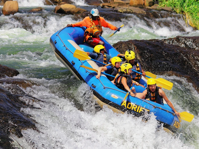 Groep reizigers in een opblaasbare raft met helmen en peddels, die samen een wilde rivier afvaren tussen de rotsen.