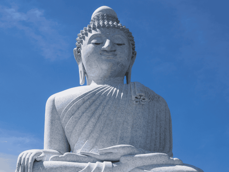Witte Boeddhabeeld van marmer tegen een heldere blauwe lucht.