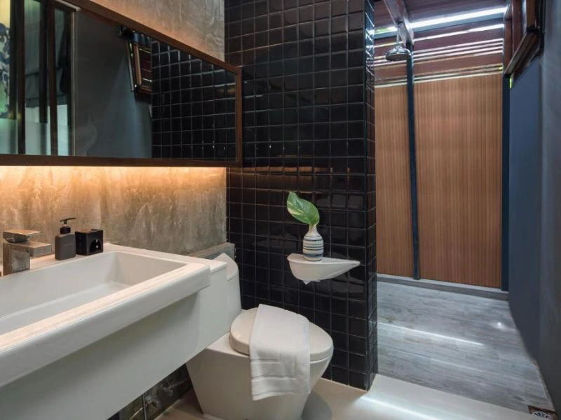 Modern ingerichte badkamer met zwart tegelwerk, inloopdouche en wastafel met spiegelwand.