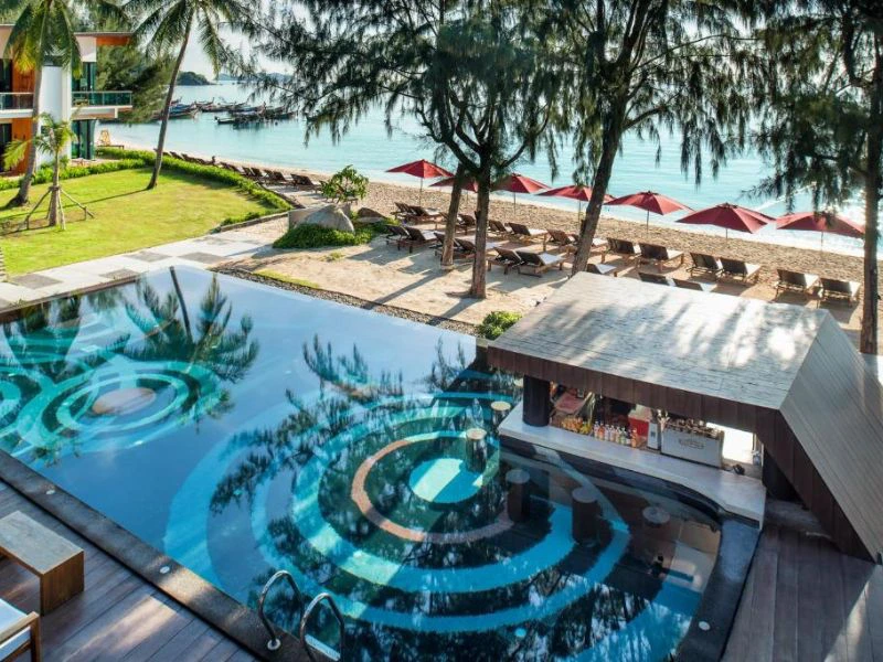 Zwembad met bar en designpatroon aan tropisch strand met ligbedden en parasols.