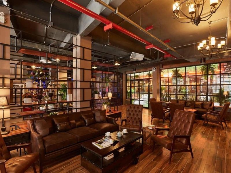 Een sfeervolle lounge met leren banken en stoelen, warme verlichting en een industriële look door het open plafond en metalen rekken.