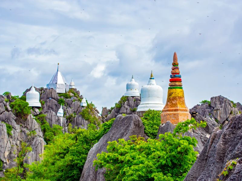 Witte stoepa’s en een kleurrijke pagode op grillige rotspieken tussen het groen, onder een bewolkte hemel.