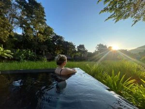 Vrouw staand in een zwembad uitkijkend over de rijstvelden in Mae Hong son in Noord-Thailand. De zon schijnt op haar gezicht.