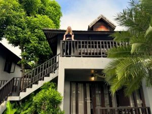 Vrouw staand op een balkon van een huisje dat hoort bij een kleinschalig resort in Pai, Noord-Thailand. Het huisje staat tussen groene bomen en is gemaakt van hout en beton.