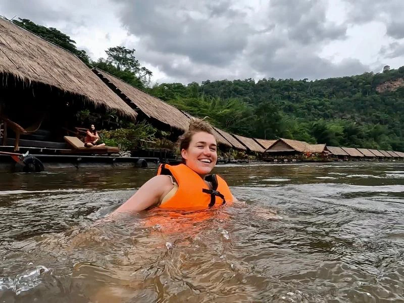 vrouw met zwemvest aan dobberend in River Kwai. De drijvende houten huisjes zie je op de achtergrond.