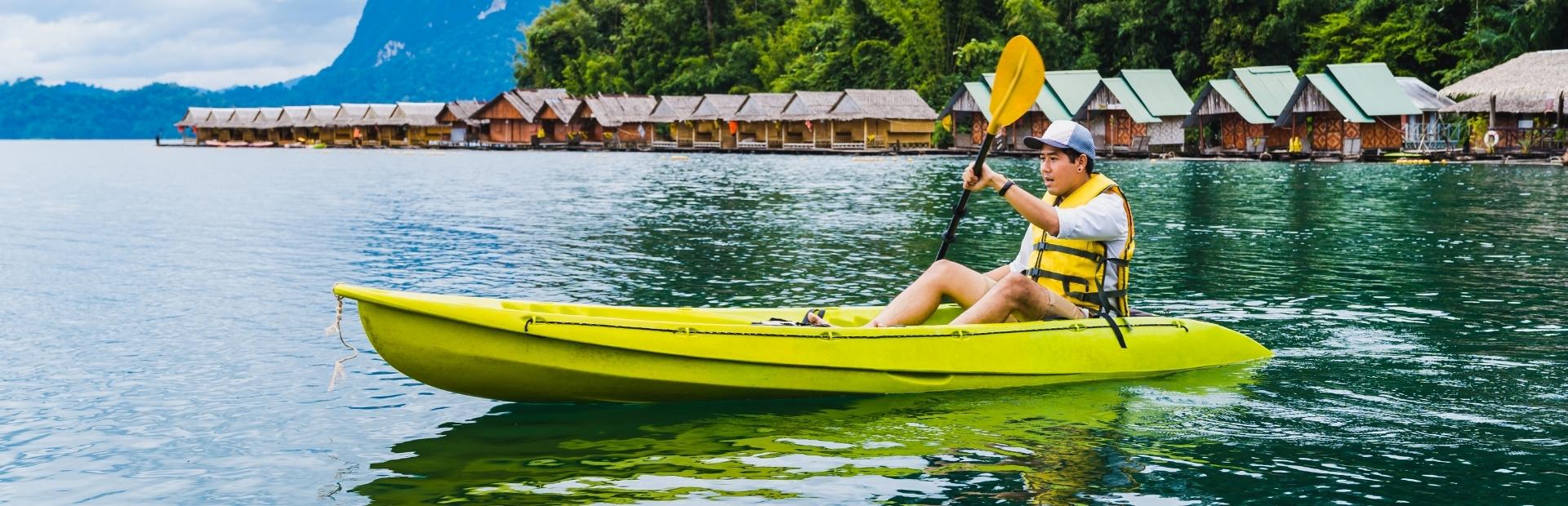 Man kajakkend door Cheow Lan Lake in Khao Sok, Thailand. Op de achtergrond zie je bungalows op het water.