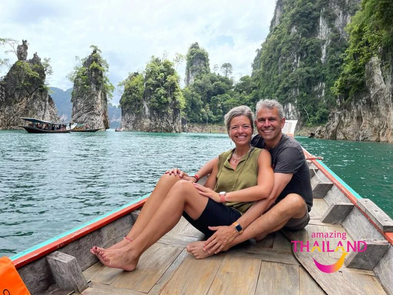 Een koppel zit ontspannen op een houten boot tussen groene rotsformaties op helder blauw water in Khao Sok op het meer van Cheow Lan.
