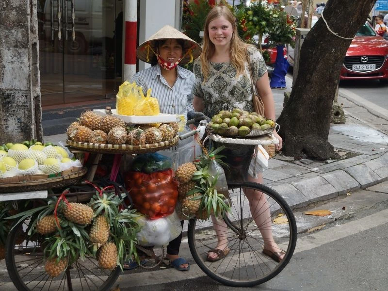 Reiziger en lokale vrouw staan bij een fiets, die vol hangt met lokaal fruit.