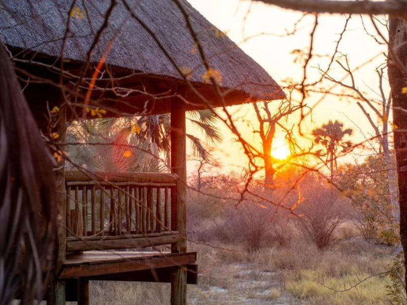 Houten hut met rieten dak in een droog landschap bij zonsondergang.
