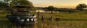 Drie mensen op een stoeltje kijken uit over een meer in Limpopo. Een man staat naast hen en daarnaast staat de safari auto.