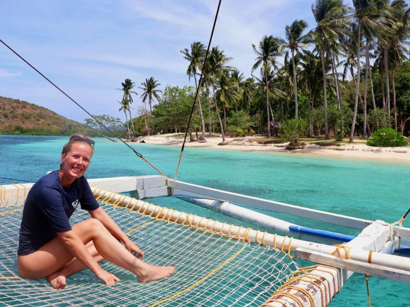vrouw zit op boot met blauw water en palmbomen