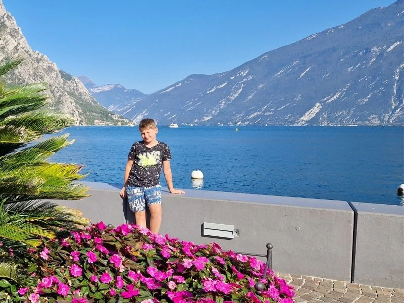 Kind bij blauw gardameer met bergen en bloemen op de achtergrond