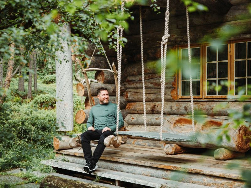 Reiziger zit op een schommel voor een cabin.