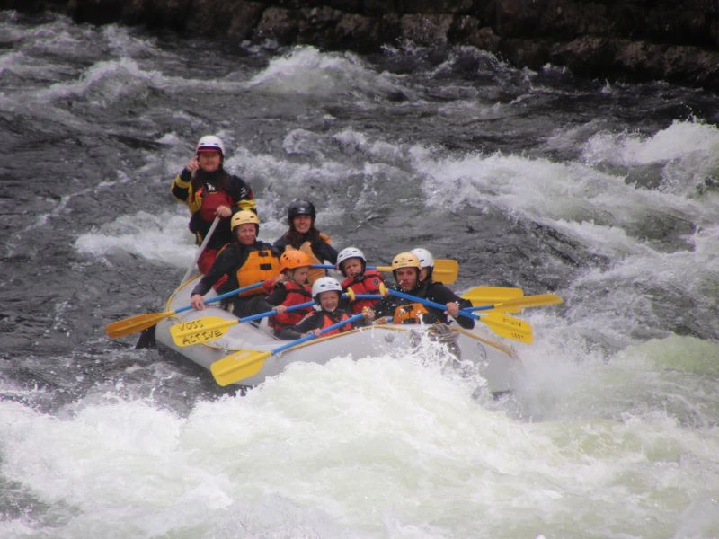 Familie zit in een gele boot en is aan het raften op een wildwaterrivier in Noorwegen.