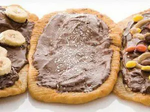 Drie stukken gefrituurd deeg belegd met chocoladespread, één met banaan, één met gekleurde snoepjes en één enkel met poedersuiker.