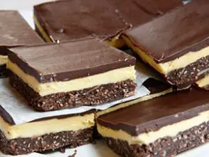 Stukken Nanaimo bars, bestaande uit drie lagen: een krokante bodem van koek en noten, een romige vanillevulling en een glanzende laag pure chocolade erbovenop.