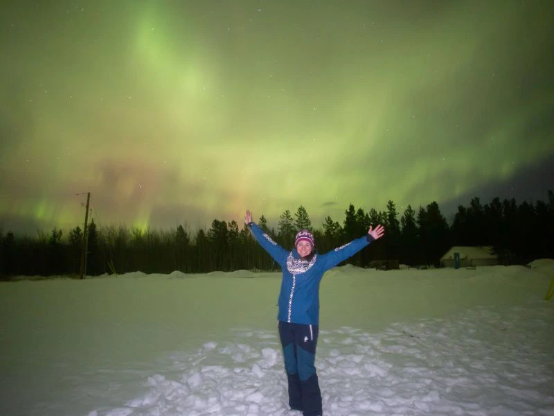 Reiziger staat in de sneeuw. Op de achtergrond zie je het noorderlicht in Canada.