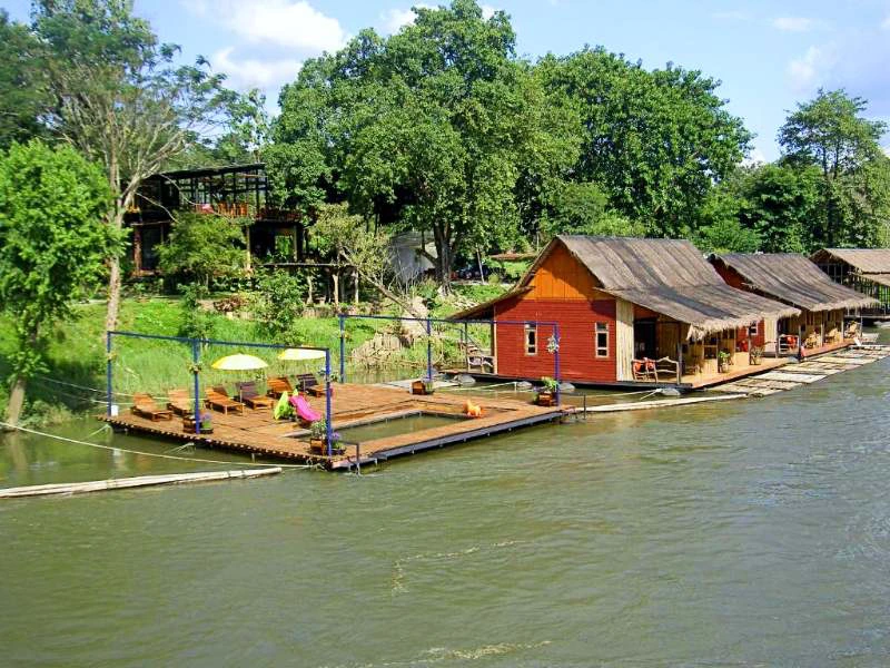 Drijvende houten huisjes en zonnedek aan een groene rivier.