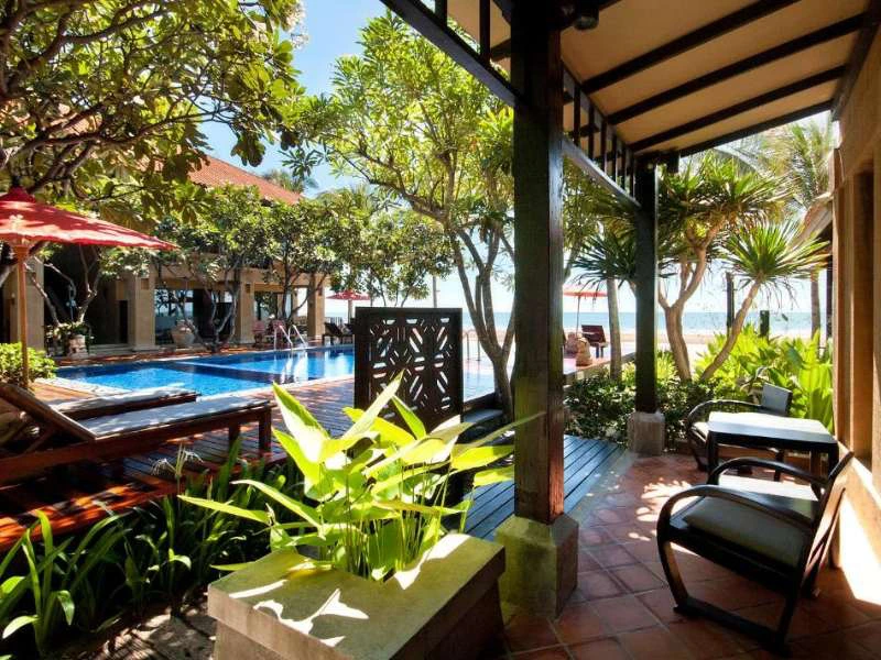 Tropisch resort met zwembad en uitzicht op zee, omringd door palmbomen en loungeplekken.