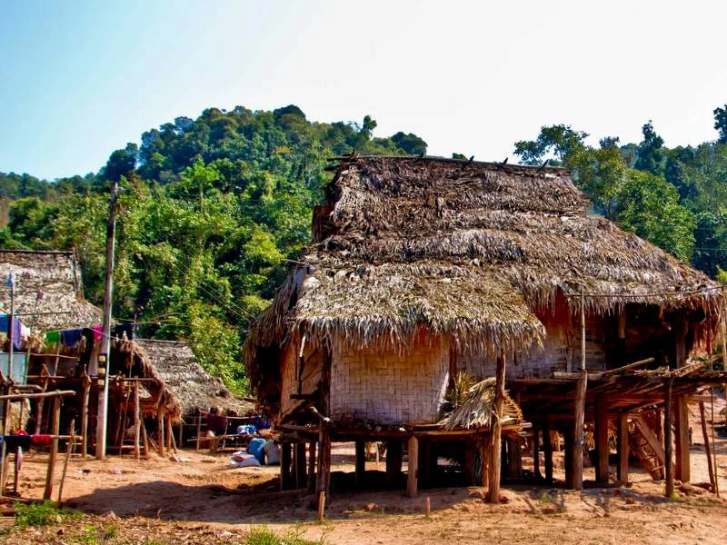 Traditionele houten paalwoningen met daken van palmbladeren in een bergachtig dorp omringd door groene jungle.