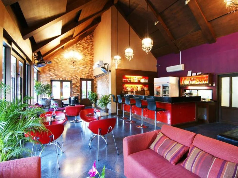 Modern ingerichte bar en lounge met hoge houten plafondbalken, rode stoelen en banken, hanglampen en een lange zwarte bar met barkrukken.