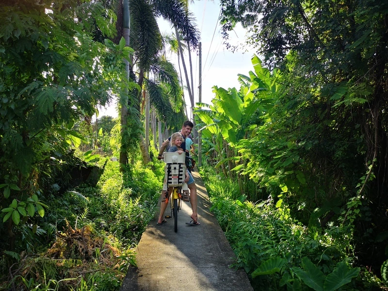 Vader en dochter fietsen samen over een smal paadje door weelderige tropische jungle.