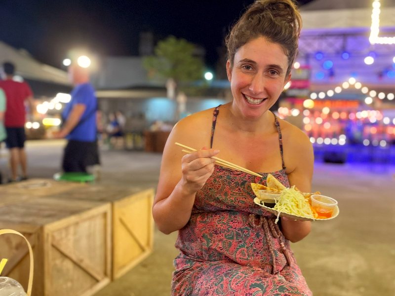vrouw eet streetfood met chopsticks op een avondmarkt.