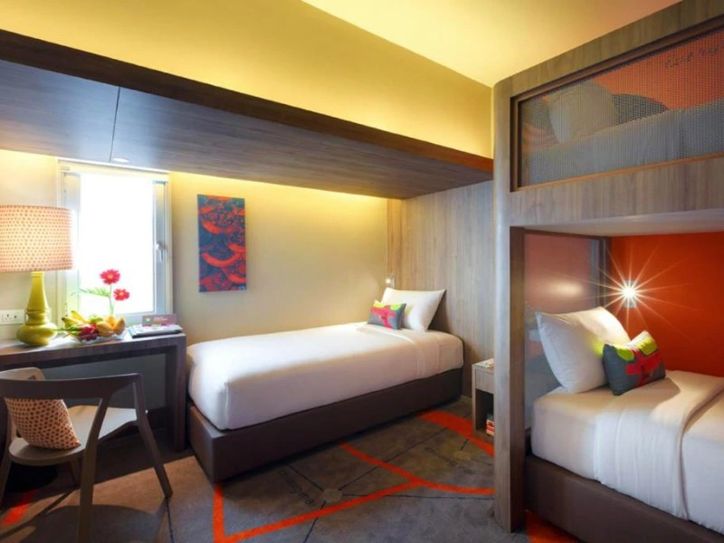Moderne hotelkamer met drie eenpersoonsbedden, bureau en kleurrijke accenten.