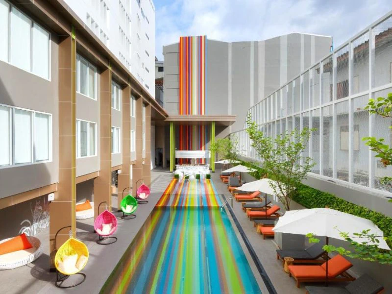 Modern hotelzwembad met kleurrijke strepen, ligstoelen en hangstoelen.