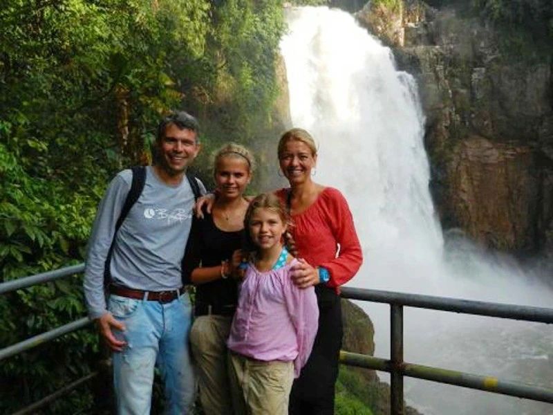 Gezin poseert lachend voor een grote waterval omringd door weelderige jungle.