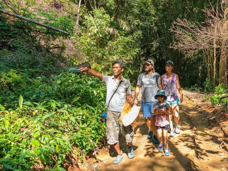 Gezin met vader, moeder en dochter, allemaal met hoofddeksel op, volgen een lokale gids in de jungle van Thailand.