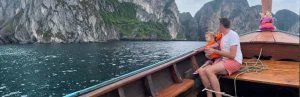 Vader en jong kind in een houten longtailboot op zee bij de rotsachtige, groene kliffen van Koh Phi Phi in Thailand.