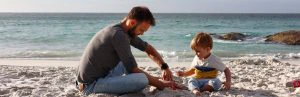 Man met een klein jongetje zitten op het strand in Zuid-Afrika met de zee op de achtergrond