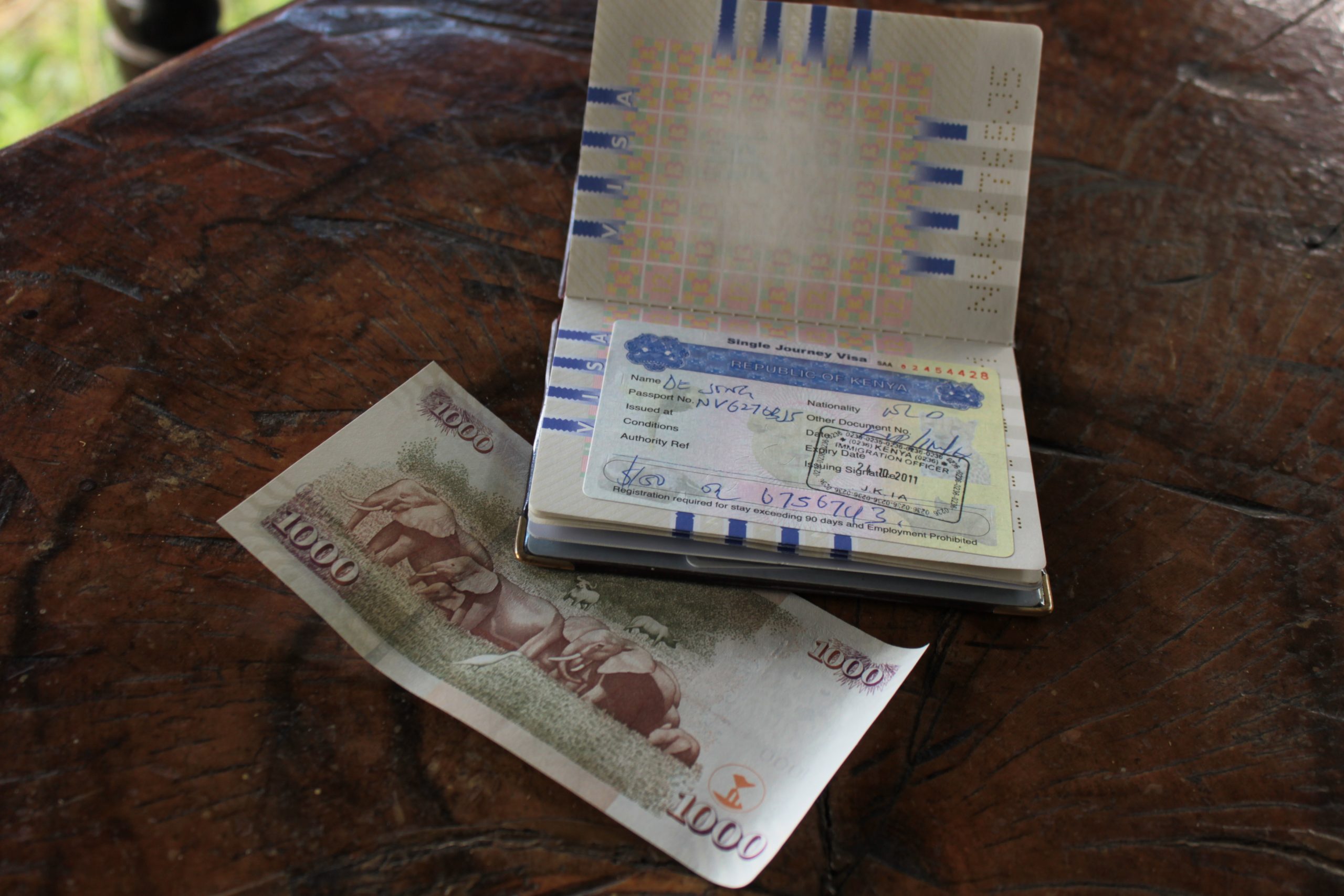 Paspoort met visumstempel en een biljet van 10.000 Oegandese shilling op een houten tafel.