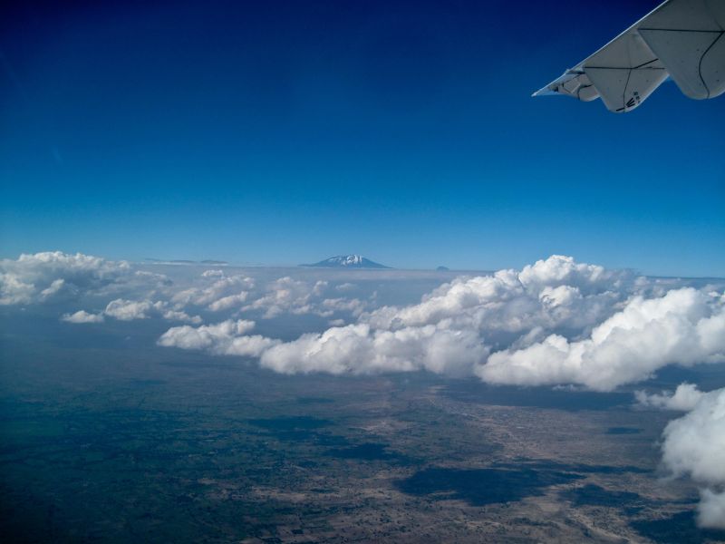Foto vanuit het vliegtuig met wolken op de voorgrond en uitzicht over de Kilimanjaro