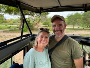 Foto van vrouw en man vanuit open jeep met giraffen op de achtergrond