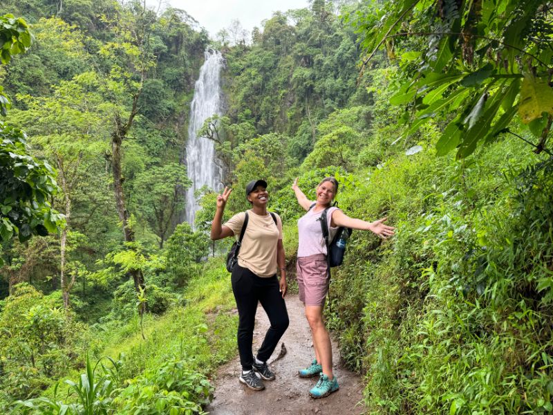 Vrouw en gids poseren voor de waterval meet veel groen op de achtergrond