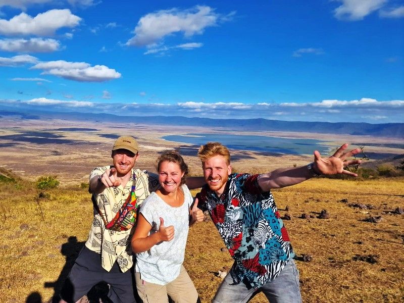 Drie mensen poseren lachend op de rand van de Ngorongoro krater, met uitzicht over de krater