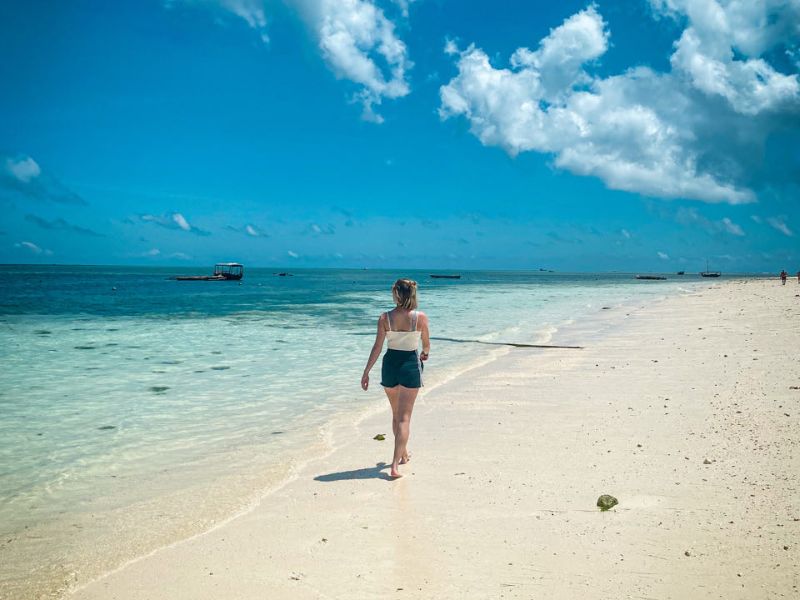 Vrouw wandelt op het strand op Zanzibar langs het azuurblauwe water