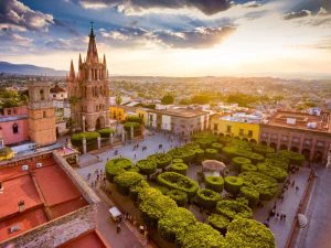 Luchtfoto van een plein in San Miguel de Allende met een kerk, een parkje in het midden en gekleurde huizen er om heen