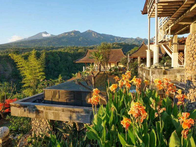 Familiehotel in Senaru op Lombok met oranje bloemen op de voorgrond en daarachter een infinitypool en bergen met heel veel groen ervoor. De lucht is helderblauw.