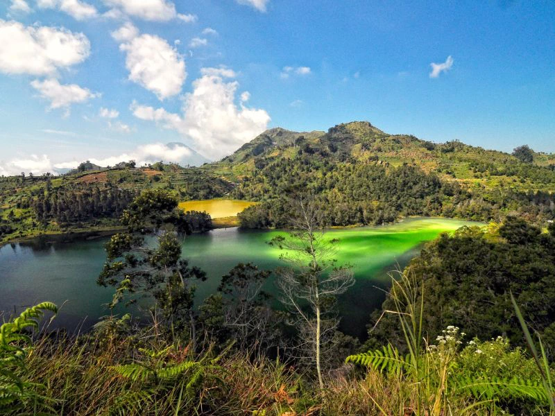 Uitzicht op het meer en de groene heuvels van het Dieng Plateau in Indonesië, met helderblauwe lucht en wolken erboven.