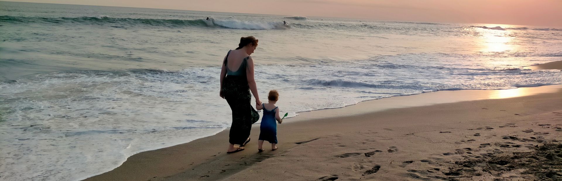 Moeder en dochtertje lopen op het zandstrand langs de kalme zee met zonsondergang.