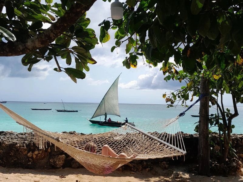 Jonge reiziger ligt in een hangmat aan het strand met op de achtergrond een traditionele dhow.