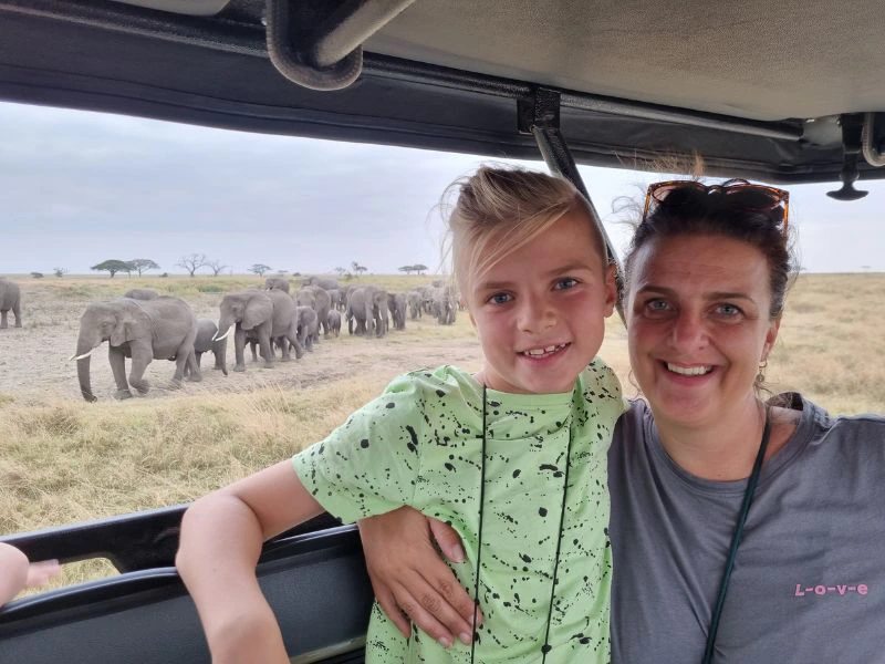 Moeder en dochter in de jeep tijdens een safari met olifanten op de achtergrond.