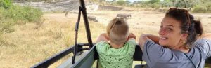Moeder en zoon kijken uit de jeep en spotten olifanten en giraffen.