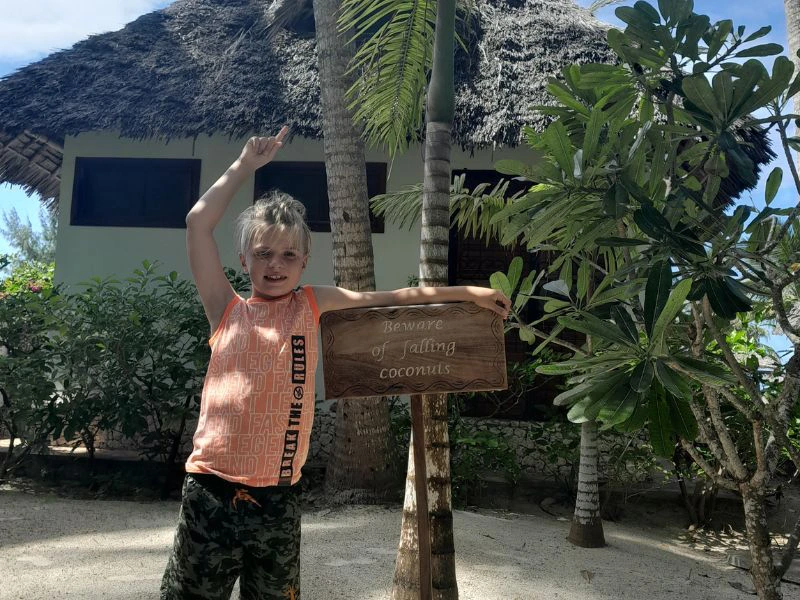 Jonge reiziger staat bij een bord 'Beware of falling coconuts' op Zanzibar.