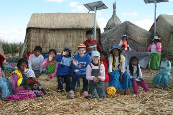 Groep kinderen zit en speelt samen voor rieten huizen op de drijvende eilanden van het Titicacameer.