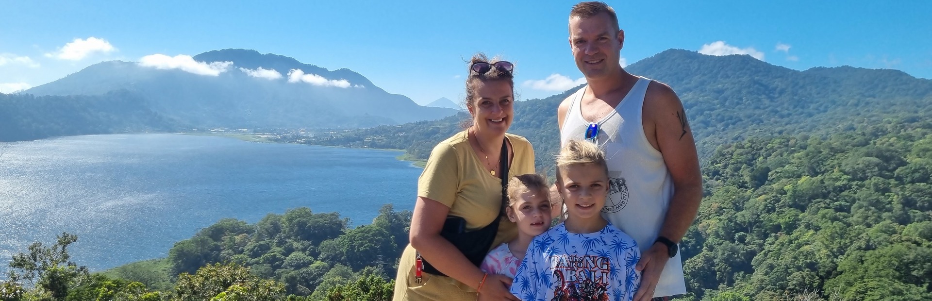 Gezin van vier poseert voor een panoramisch uitzicht op een meer en groene bergen.