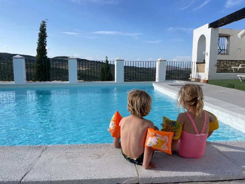 Twee kleine kindjes zittend aan de rand van een zwembad in Spanje met uizicht over heuvels.